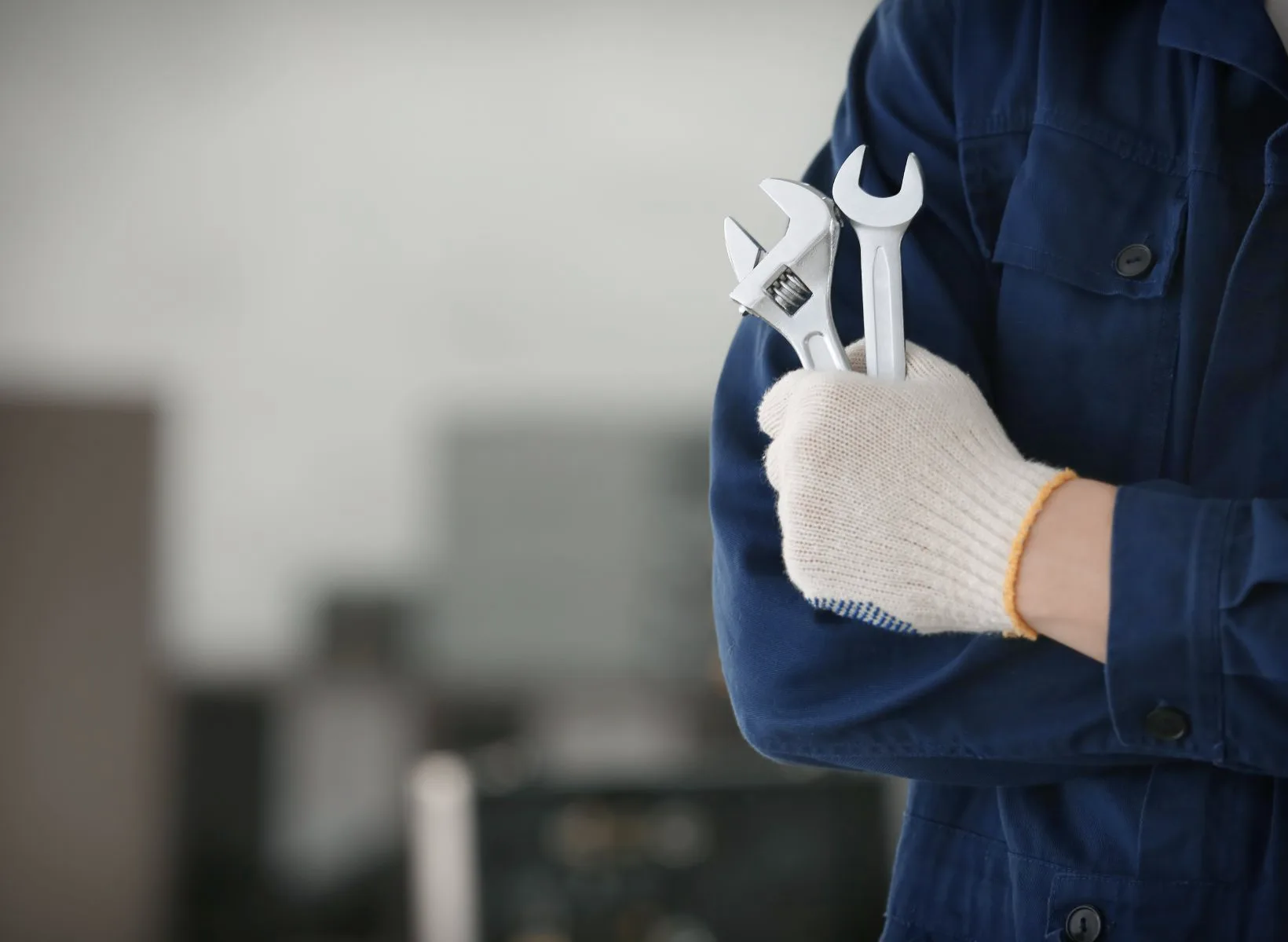 A technician with a focus on his gloved hand holding a crescent wrench and metric wrench.