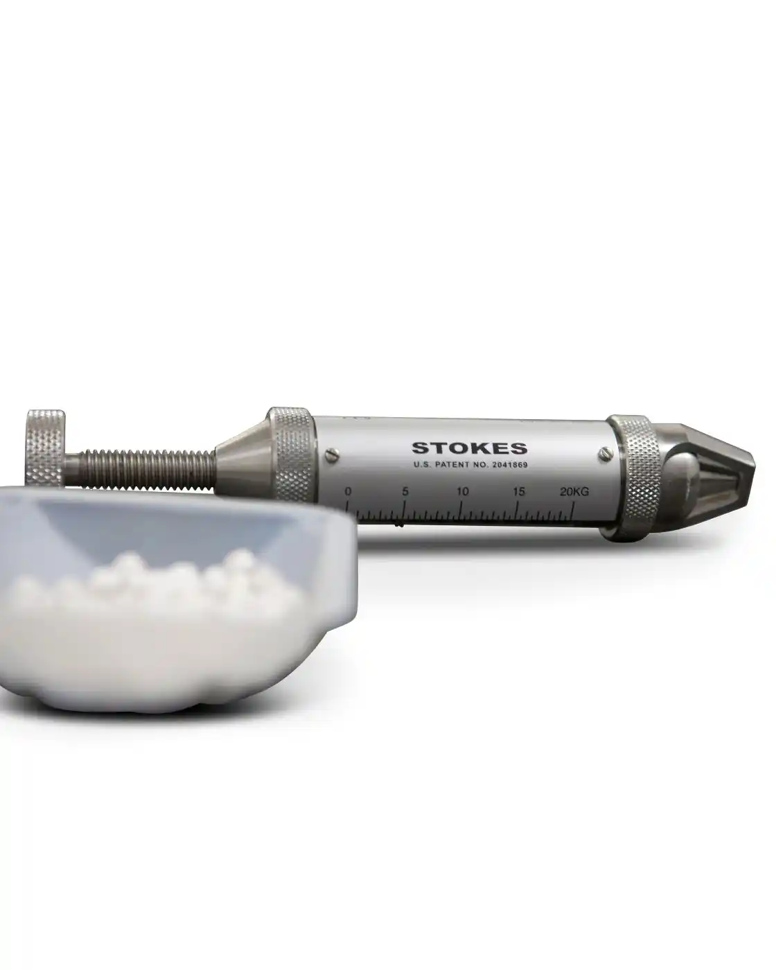 Stokes Tablet Hardness Tester next to a small container of white tablets.