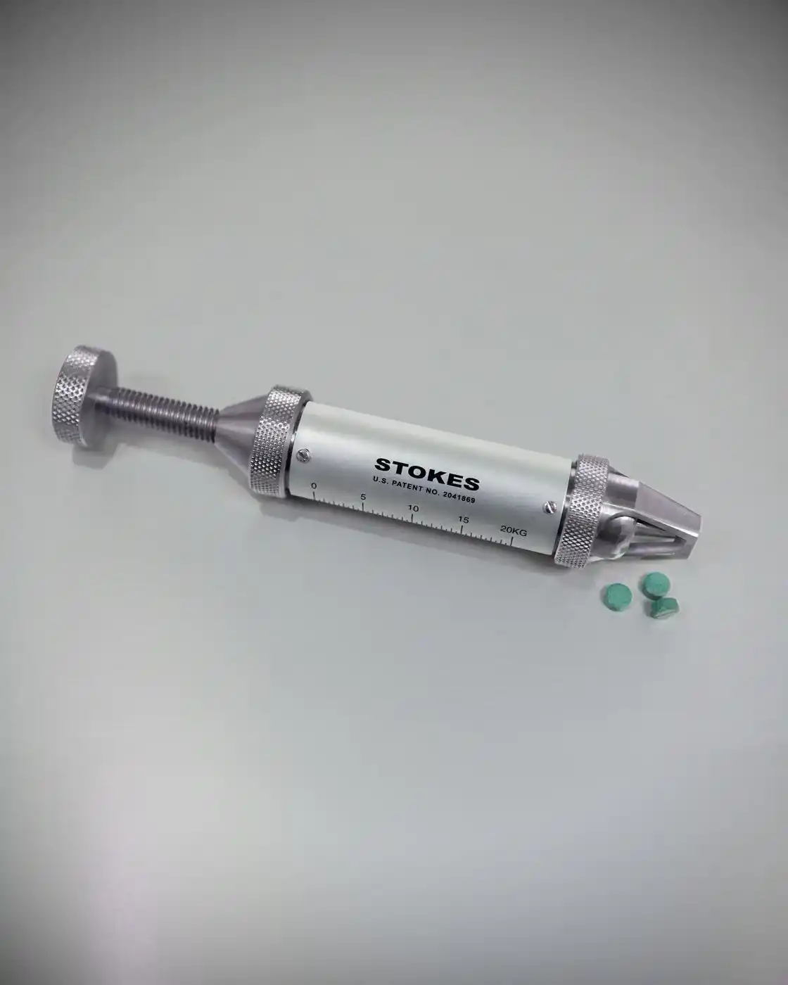 Stokes Tablet Hardness Tester next to a few green tablets.