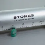 A close up shot of a Stokes Tablet Hardness Tester next to two green tablets.
