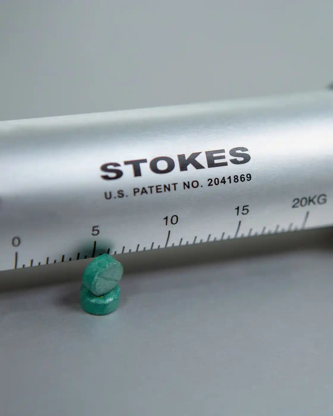 A close up shot of a Stokes Tablet Hardness Tester next to two green tablets.