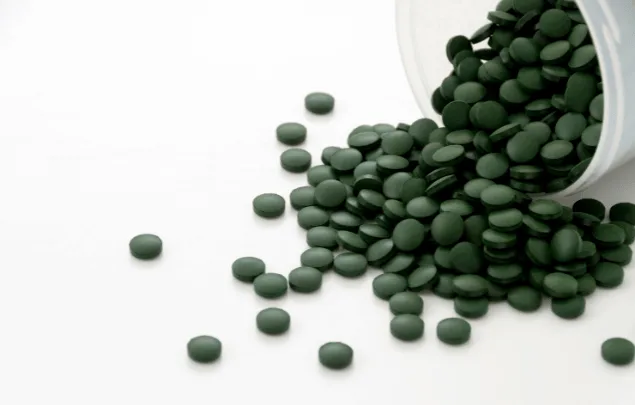 Green round tablets spilling out of a container against a white background.