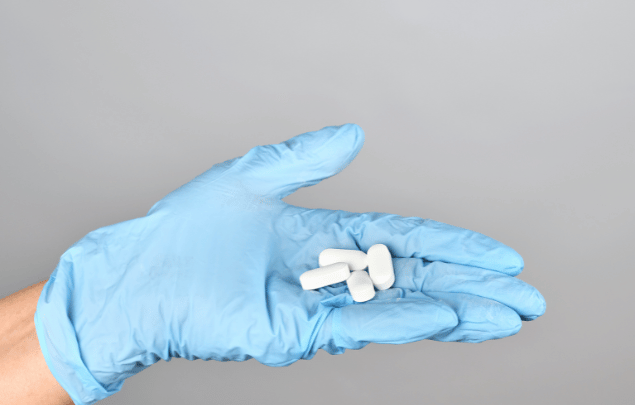 A gloved hand holding perfectly manufacturing white caplets.
