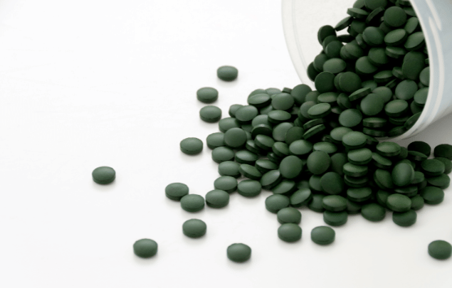 Green round tablets spilling out of a container against a white background.