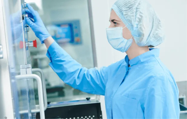 A rotary tablet press machine operator adjusting the machine. She is wearing PPE such as a hairnet, face mask, and gloves.