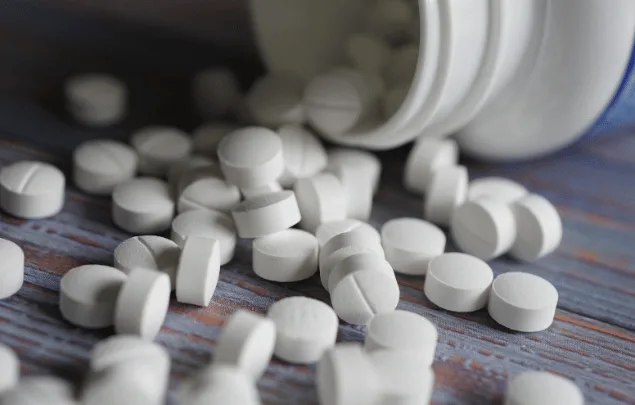 White bisected tablets tumbling out of an overturned pill bottle.